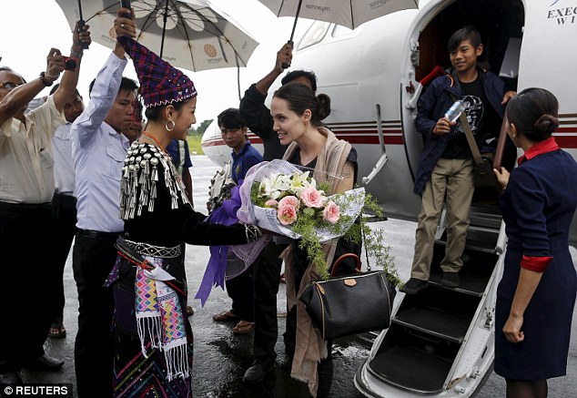 Warm welcome: Representatives from Kachin state wear traditional dress as they greet Angelina with flowers as she gets off the plane with her son Pax